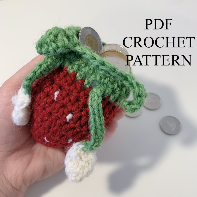 Pode incluir: Uma bolsa de morango de croch&ecirc;, cheia de moedas. A bolsa &eacute; vermelha com detalhes brancos, folhas verdes e detalhes brancos. O texto "PDF CROCHET PATTERN" &eacute; vis&iacute;vel.