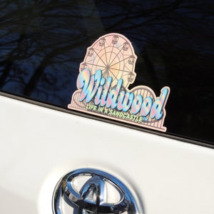 May include: A pink and blue iridescent sticker with a Ferris wheel and the text "Wildwood Life in a Sandcastle" on a white car.
