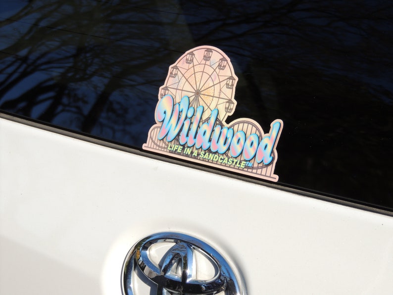 May include: A pink and blue iridescent sticker with a Ferris wheel and the text "Wildwood Life in a Sandcastle" on a white car.