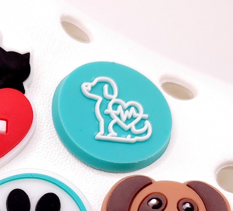 May include: A teal blue round charm with a white outline of a dog with a heart and EKG symbol inside.