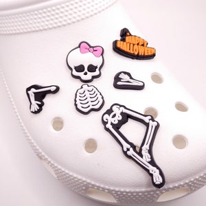 May include: A set of Halloween-themed shoe charms featuring a skeleton, a skull with a pink bow, a witch's hat, and the words "Happy Halloween".