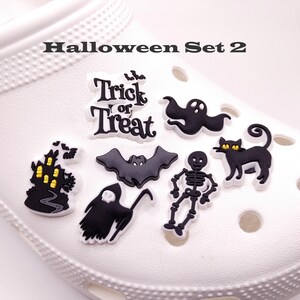 K&ouml;nnte beinhalten: Halloween-Schuhcharms mit einem Geist, einer Fledermaus, einem Skelett, einer schwarzen Katze, einem Spukhaus und einem "Trick or Treat"-Charm.