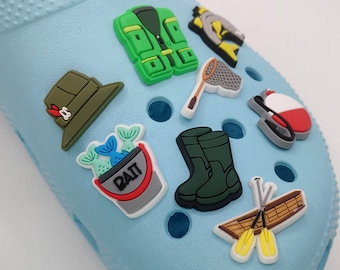 Op de afbeelding: Een set van negen kleurrijke visscharms voor schoenen. De charms omvatten een vissersvest, een visnet, een hengel, een emmer aas, een paar visserslaarzen, een dobber, een hoed en twee peddels.