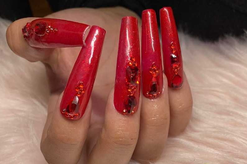 K&ouml;nnte beinhalten: Rote, lange, sargf&ouml;rmige Acryln&auml;gel mit rotem Glitzer und Strasssteinen.