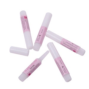 Op de afbeelding: Vijf witte buisjes nagellijm met roze etiketten. De etiketten hebben de tekst "Nail Glue" en "Caution". De buisjes zijn elk 1 gram.