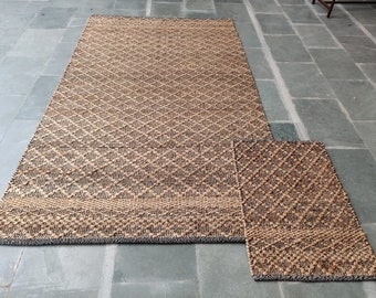 May include: A brown and black woven rug with a diamond pattern. The rug is made of natural fibers and has a fringed edge.