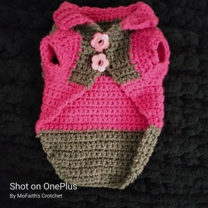 May include: A pink and brown crocheted dog sweater with a collar and two pink flower buttons. "Shot on OnePlus" and "By MoFaith's Crotchet" are written below the sweater.