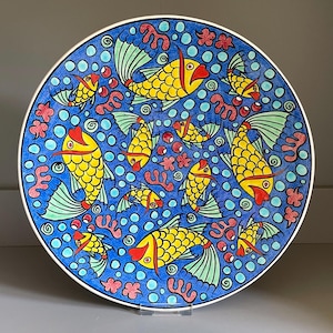 May include: A blue and white ceramic plate with a colourful design of yellow fish swimming in a blue sea with red coral and bubbles.