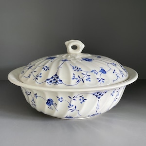 May include: A white ceramic lidded serving bowl with a fluted, ribbed texture. The exterior and lid are decorated with a delicate blue floral pattern featuring small leaves, vines, and blossoms. The lid includes a central loop-shaped handle.