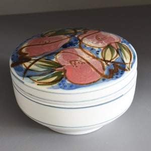 May include: A white ceramic jar with a lid. The lid is decorated with a blue and white floral design featuring pink flowers. The jar has a blue stripe around the top.