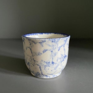 May include: A small, white ceramic egg cup with a blue marbled design.