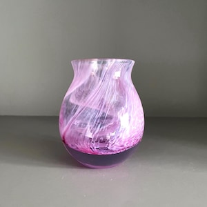 Peut inclure: Un petit vase rond à large ouverture. Le verre est tourbillonnant avec des nuances de rose et de blanc, avec une base violet foncé. Le vase a une finition lisse et polie et est probablement fait à la main.
