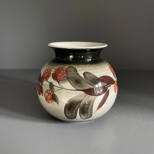 May include: A white ceramic vase with a black rim and a floral design in shades of brown and red.