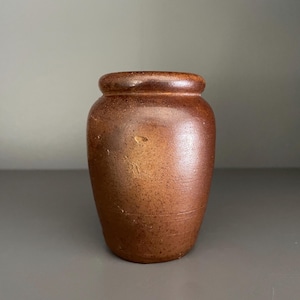May include: A brown ceramic vase with a speckled glaze. The vase has a rounded body and a slightly flared lip.