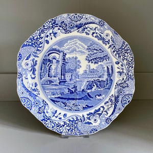 Puede incluir: Un plato de porcelana azul y blanco con un borde floral decorativo y una imagen central de un paisaje con un puente, ruinas y árboles.