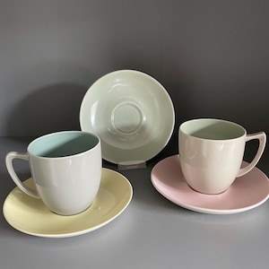 以下が含まれることがあります： パステルカラーのセラミックティーカップとソーサーの3点セット。カップはグレーで内側は水色、黄色のソーサーに乗っています。もう一つのカップはベージュで、ピンクのソーサーが付いています。薄緑色のソーサーも存在します。