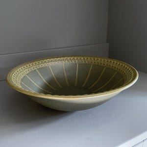 Puede incluir: Una taza de cerámica blanca con un asa negra y el texto "But First, Coffee" en negro y negrita. La taza está sobre una superficie de madera. La taza mide 10 cm de alto.