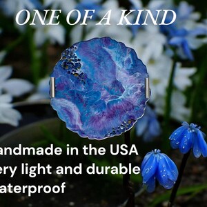 May include: A round, blue and purple decorative piece with silver handles, set against a blurred floral background. The text "ONE OF A KIND" is at the top. The piece is handmade in the USA, very light and durable, and waterproof.