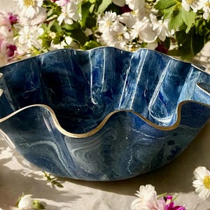 May include: A decorative blue and white marbled bowl with a ruffled edge and gold trim. The bowl is surrounded by white and pink flowers, creating a visually appealing contrast.
