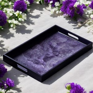 Puede incluir: Una bandeja rectangular para servir con marco negro y superficie de mármol morado. La bandeja tiene dos asas a los lados.