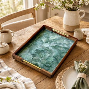May include: A rectangular wooden serving tray featuring a dark brown frame and two gold-toned metal handles. The base of the tray displays a vibrant, swirling green and white pattern that resembles the appearance of rippling water or marble.
