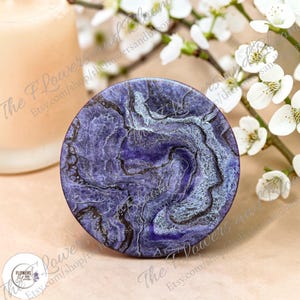 May include: A circular coaster featuring a deep purple and black marbled resin design with swirling white accents. The surface has a glossy finish with intricate, vein-like patterns that mimic natural stone, creating a textured appearance.
