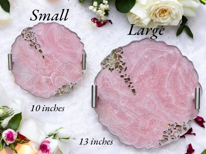 May include: Two pink resin serving trays with silver handles. The smaller tray is 10 inches in diameter and the larger tray is 13 inches in diameter. Both trays have a marbled design with gold flecks.