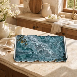 May include: A rectangular serving tray featuring a fluid, marbled design in shades of deep teal, navy, and white, mimicking ocean waves. The tray has a jagged, organic edge and is fitted with two long, cylindrical silver-toned metal handles.