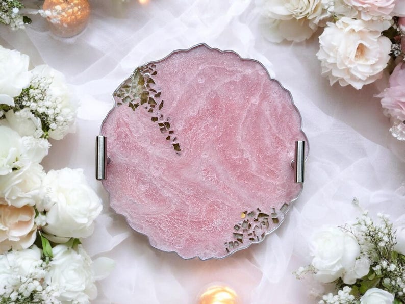 May include: A round pink resin serving tray with a scalloped edge and silver handles. The tray has a marbled effect and gold flecks throughout.