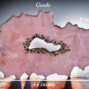 May include: A pink resin geode with a clear crystal center, measuring 14 inches wide and 8 inches tall. The geode has a unique, organic shape and is perfect for adding a touch of nature to any home decor.