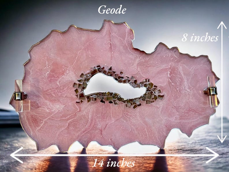 May include: A pink resin geode with a clear crystal center, measuring 14 inches wide and 8 inches tall. The geode has a unique, organic shape and is perfect for adding a touch of nature to any home decor.
