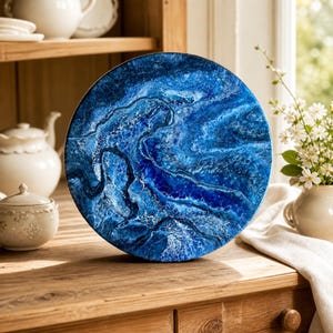 May include: A circular decorative art piece featuring a swirling abstract pattern in deep shades of navy, royal blue, and white. The surface has a glossy, resin-like finish with textured, wave-like ridges that mimic the appearance of ocean water.