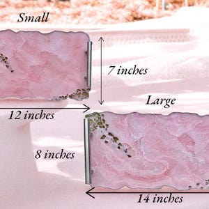 May include: Two pink resin serving trays with gold flecks. The smaller tray measures 12 inches by 7 inches. The larger tray measures 14 inches by 8 inches.