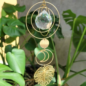 Puede incluir: Atrapasol de cristal dorado con una bola de cristal transparente, una luna creciente y un diseño de hoja. El atrapasol está colgado de una cadena.