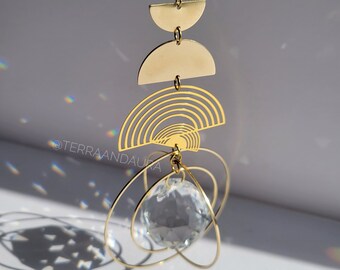 May include: Gold geometric suncatcher with a crystal prism hanging from a chain. The suncatcher features a series of overlapping circles and semi-circles.