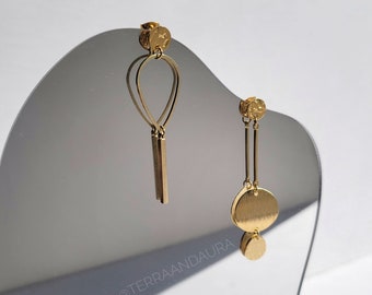 May include: A pair of gold earrings with geometric shapes. One earring features a teardrop shape with a dangling bar, while the other has a round disc and a smaller round disc below it.