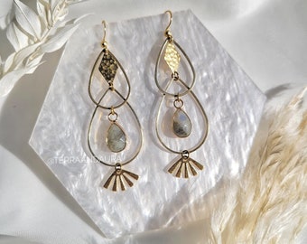 May include: Gold tone earrings with a teardrop design featuring a grey gemstone and a fan-shaped dangle. The earrings are on a white background.