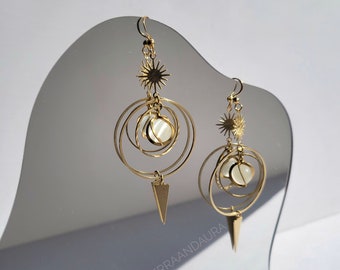 May include: Gold tone earrings with a white stone and a starburst design. The earrings are hanging from a mirror.
