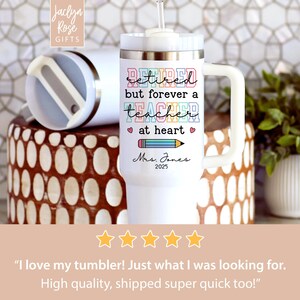 May include: White insulated tumbler with a handle and a straw. The tumbler has the text "Retired but forever a teacher at heart" with a pencil graphic. The name "Mrs. Jones" and the year "2025" are also printed on the tumbler.