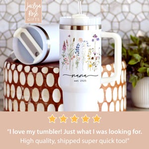 May include: White insulated tumbler with a handle, featuring a floral design and the word "nana" with "est. 2025". The tumbler has a white lid and a clear straw. The Jaclyn Rose Gifts logo is visible.