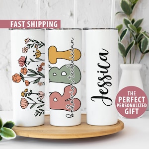 May include: Three stainless steel tumblers with different designs. The first tumbler has a floral design with pink, orange, and yellow flowers. The second tumbler has the words "Behavior Technician" written in a colorful font. The third tumbler has the name "Jessica" written in cursive.