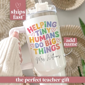 May include: White tumbler with a handle and a lid, featuring the text "HELPING TINY HUMANS DO BIG THINGS" in colorful letters. The name "Mrs. Williams" is written below. A pink heart and the words "ships fast" are in the upper left corner.