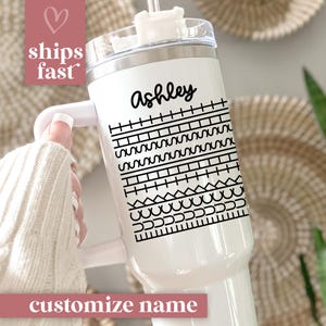 May include: White tumbler with a black geometric pattern and the name "Ashley" in script. The tumbler has a handle and a clear lid. The text "customize name" is at the bottom.