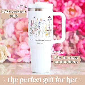 May include: White tumbler with a handle, featuring a floral design and the text "mimi est. 2025". The tumbler is labeled "Dishwasher safe" and "Fits in most cupholders".