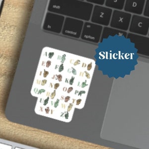 Peut inclure: Un autocollant avec l'alphabet en langue des signes. Chaque lettre est représentée par un geste de la main dans un schéma de couleurs vert, marron et or.
