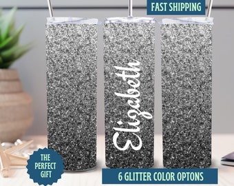 May include: A set of three glitter-covered tumblers with a silver ombre effect. The center tumbler has the name "Elizabeth" in white script. The tumblers have a straw and lid. Text on the image says "Fast Shipping", "The Perfect Gift", and "6 Glitter Color Options".