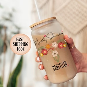 May include: A clear glass tumbler with a bamboo lid and a straw. The tumbler has a floral design and the text "Monthly Subscription CANCELLED".
