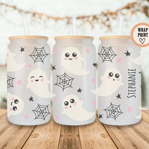May include: Three glass beverage cups with a Halloween theme. The cups feature a wrap-around print of smiling ghosts, spiderwebs, and stars in black and pink on a frosted background. Each cup has a bamboo lid and a straw.