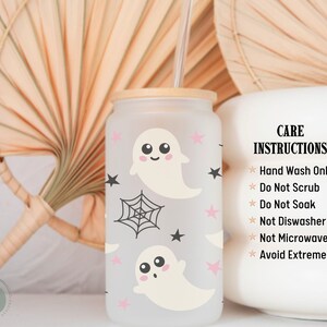 May include: A frosted glass tumbler with a bamboo lid and straw, decorated with cartoon ghosts, pink stars, and a spiderweb. The tumbler has care instructions printed on the side.