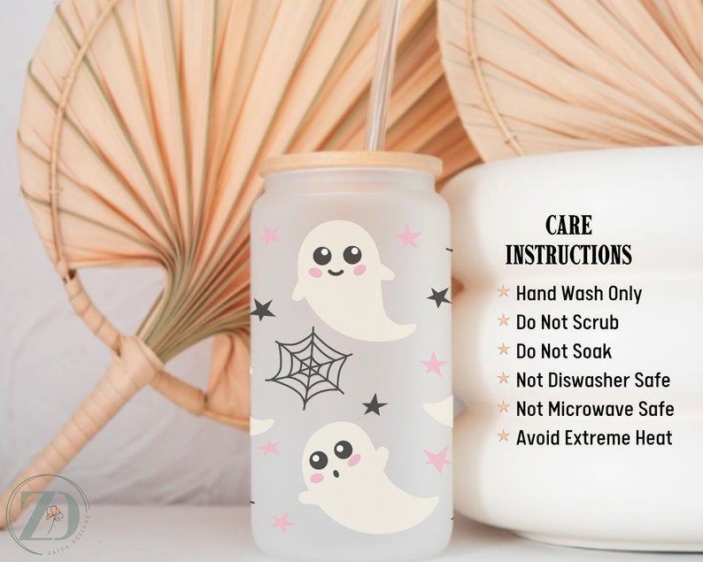 May include: A frosted glass tumbler with a bamboo lid and straw, decorated with cartoon ghosts, pink stars, and a spiderweb. The tumbler has care instructions printed on the side.